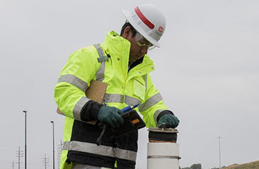 Seven pairs of piezometers are used to monitor groundwater levels beneath and adjacent to the CDF perimeter dike. Each pair of piezometers is located on the top and at the toe of the dike. The piezometer data inform conditions of dike stability with respect to groundwater elevation. A technician monitors the groundwater level at a piezometer.