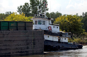 A tugboat pushes a loaded hopper barge from the dredging location to the hydraulic offloading area near the CDF, and then pushes the empty barge back to the dredging location to be reloaded.